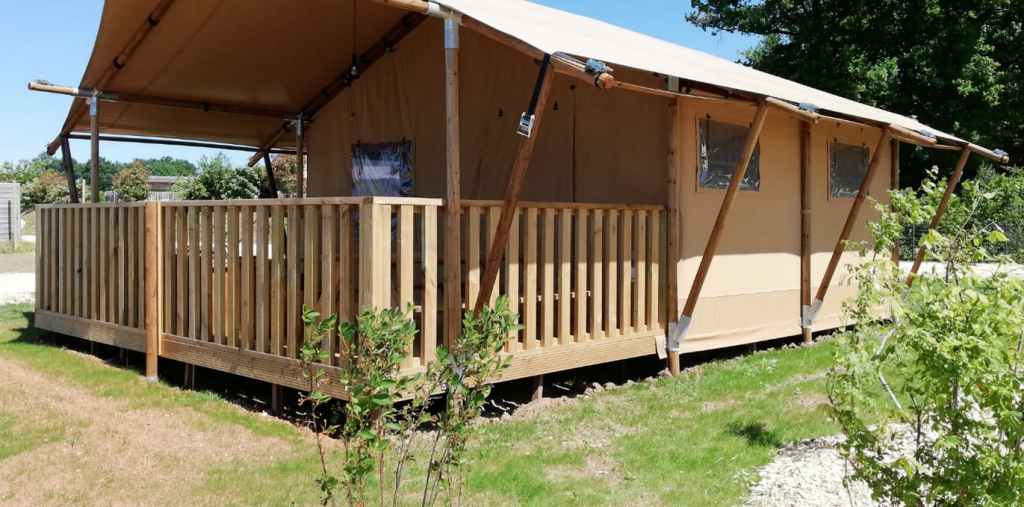 Tente safari beige avec terrasse en bois dans un espace vert