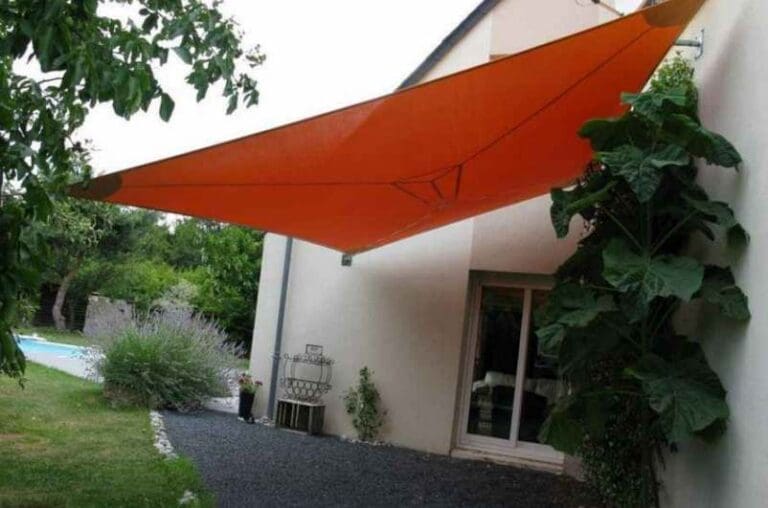 Voile d'ombrage orange tendue au-dessus d'une terrasse avec plantes au mur