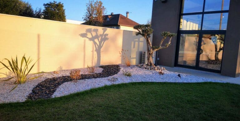 Aménagement paysager avec gravier blanc, paillis sombre et olivier devant une maison moderne