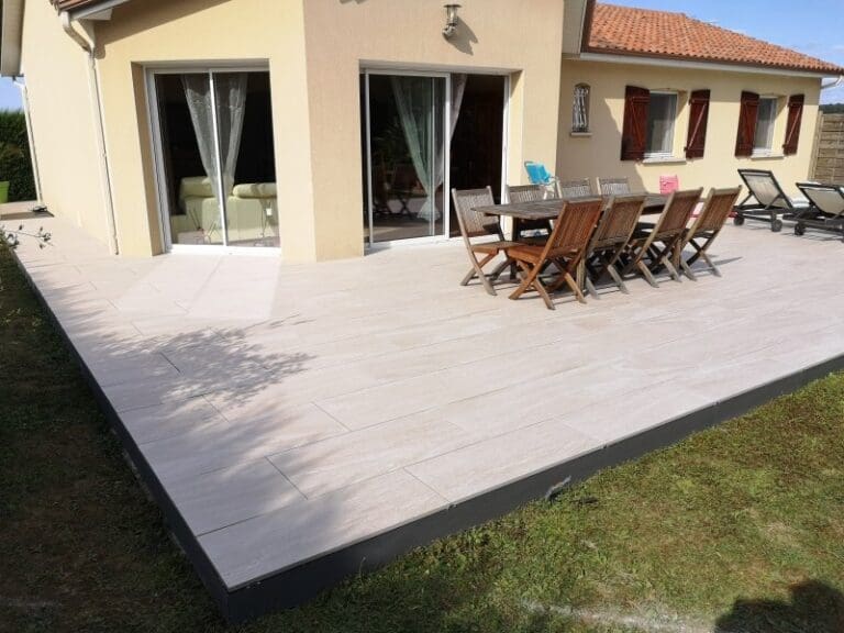 Grande terrasse en dalles claires avec table en bois et chaises devant une maison beige