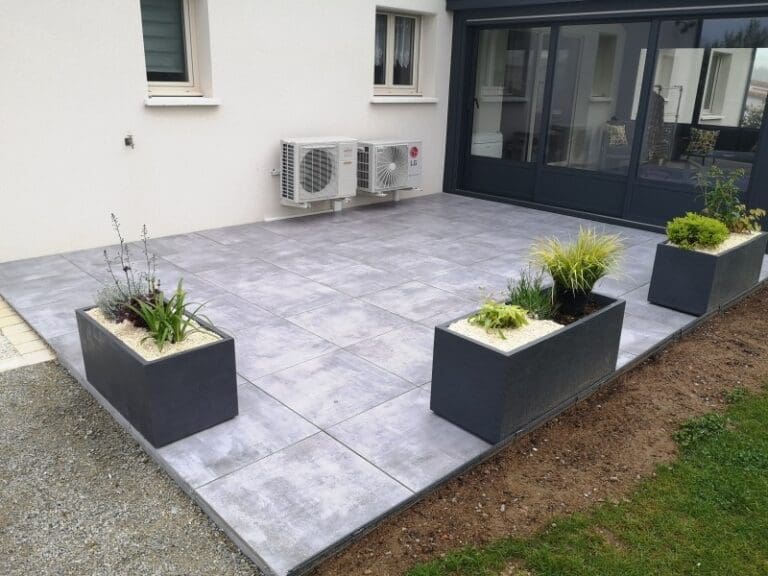 Terrasse dallée grise avec trois jardinières rectangulaires noires, plantes variées