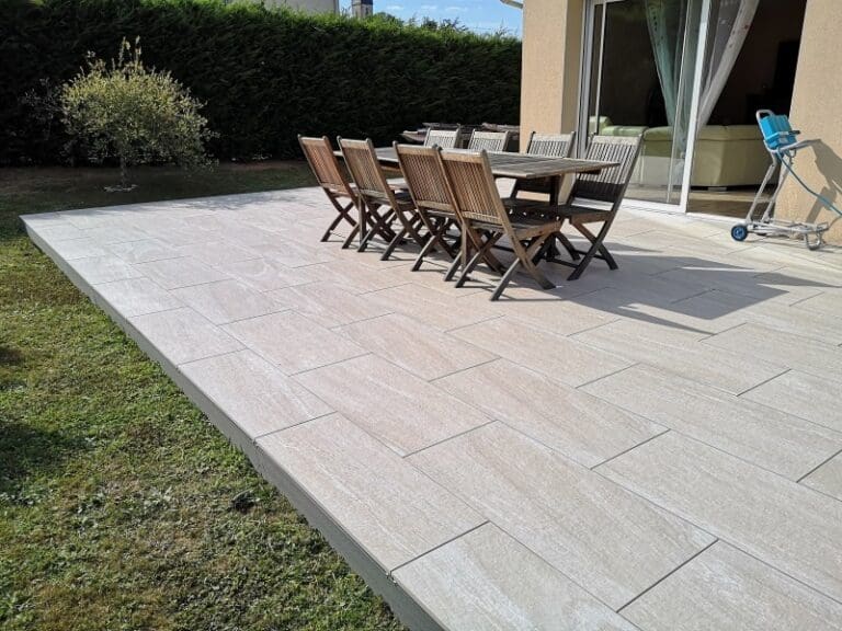 Terrasse en dalles claires avec table et chaises en bois, devant une maison