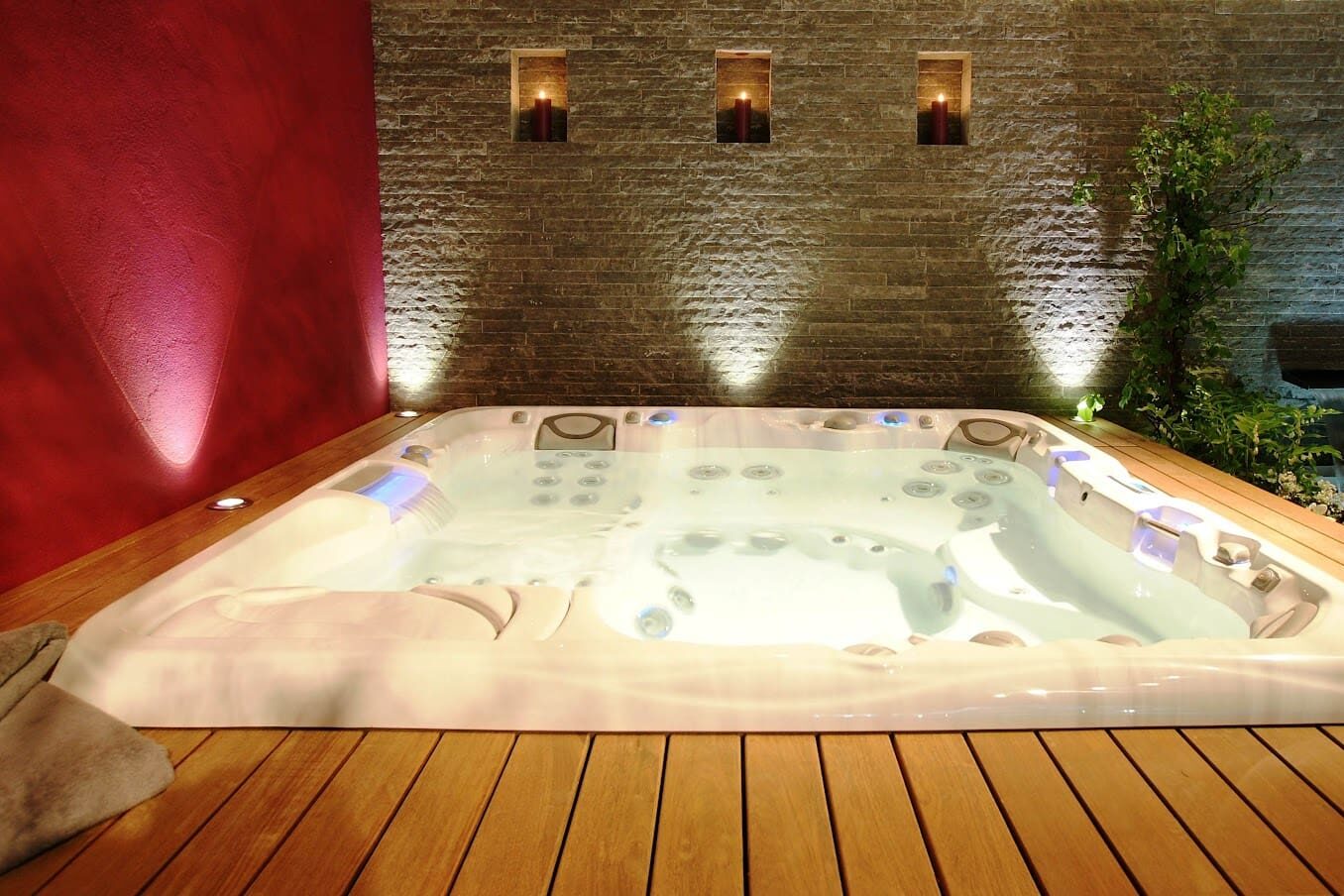 Spa blanc encastré dans une terrasse en bois avec éclairage d'ambiance et bougies murales