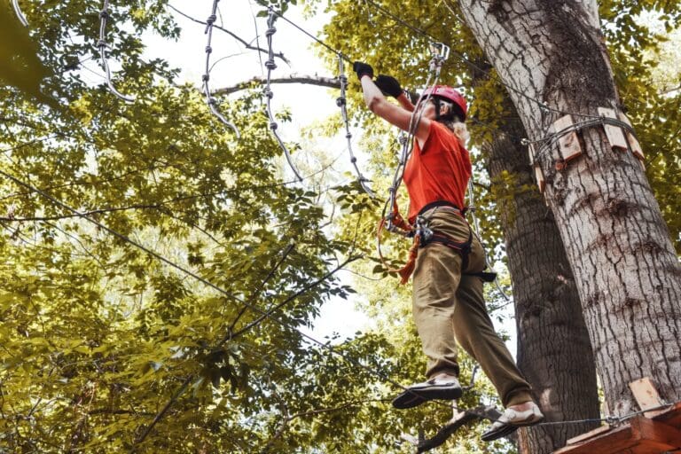 Personne avec casque rouge et harnais accroché à une tyrolienne en forêt