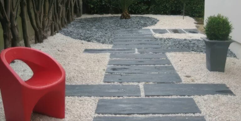 Allée moderne en dalles grises avec gravier blanc et noir, fauteuil rouge et plantes