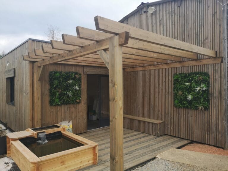 Pergola en bois avec bassin et murs végétalisés sur un patio en bois devant une maison en bardage bois