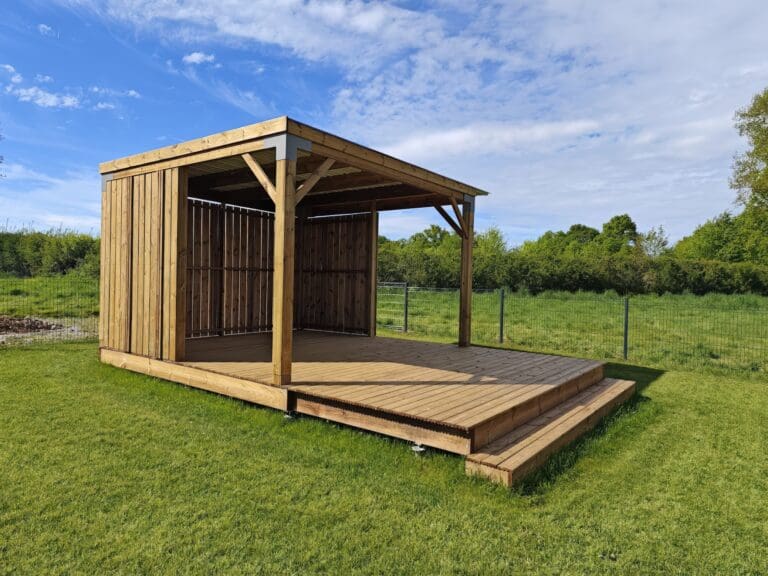 Pergola en bois avec terrasse sur pelouse sous ciel bleu partiellement nuageux