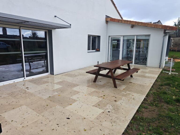 Terrasse en pierre avec table et bancs en bois devant une maison blanche