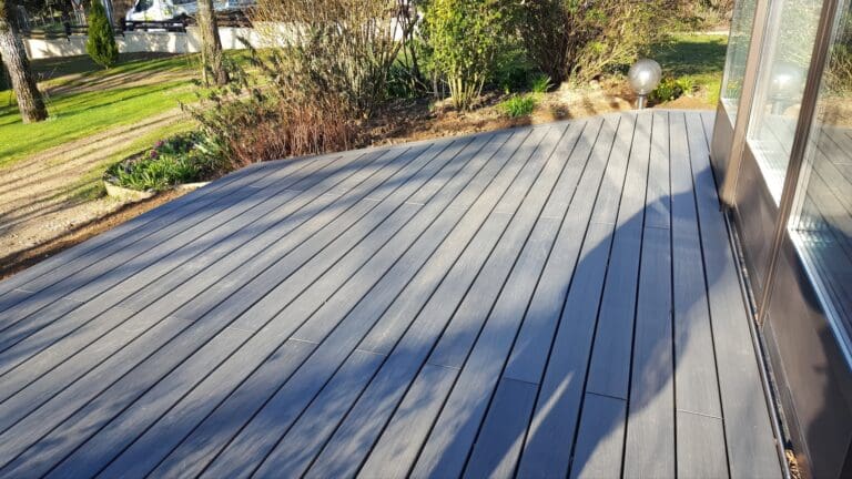 Terrasse en bois composite gris devant une baie vitrée avec jardin en arrière-plan
