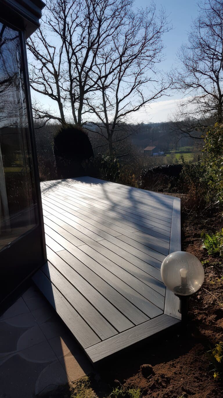 Terrasse en bois clair au soleil avec lampadaire boule et arbres en arrière-plan