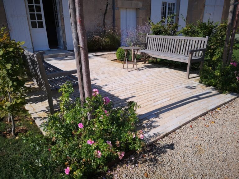 Terrasse en pierre claire avec deux bancs en bois et un petit guéridon