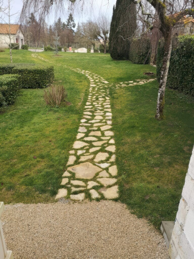 Allée en pierres irrégulières séparées par de l'herbe dans un jardin vert