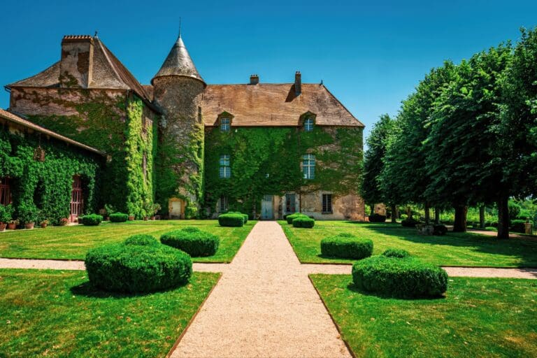 Grand bâtiment ancien en pierre avec façade couverte de lierre et jardin soigné devant