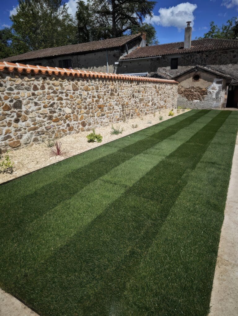 Allée de gazon nouvellement posée avec bandes ton sur ton devant un mur de pierre