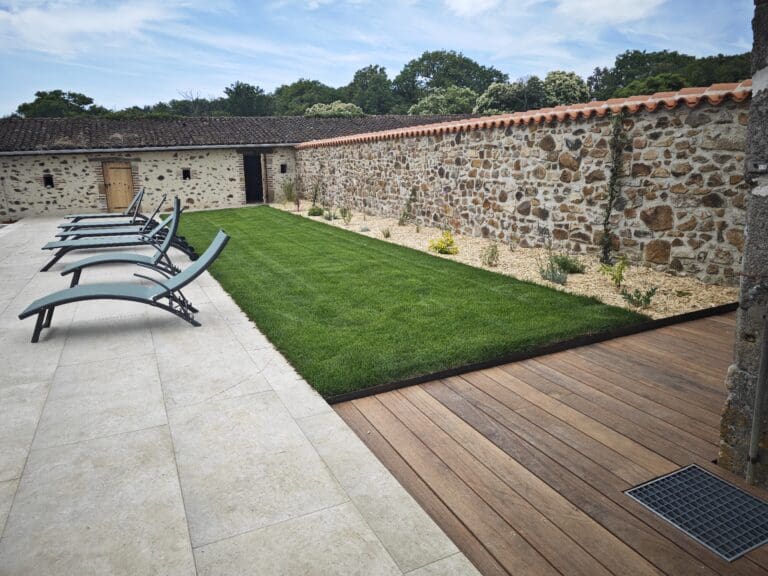 Jardin aménagé avec pelouse, bordure de plantes, terrasse en bois et transats
