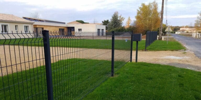 Clôture grillagée noire autour d'une parcelle avec gazon et bâtiment en arrière-plan