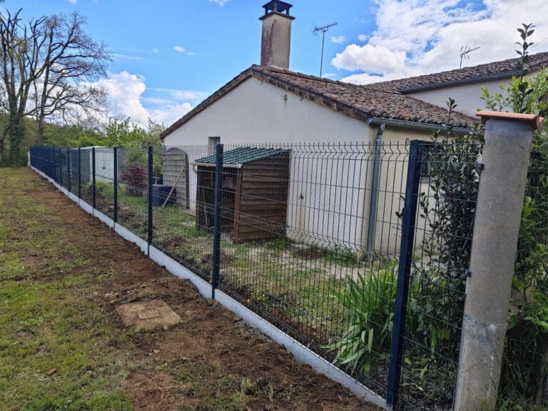 Clôture grillagée noire avec soubassement en béton le long d'une maison blanche