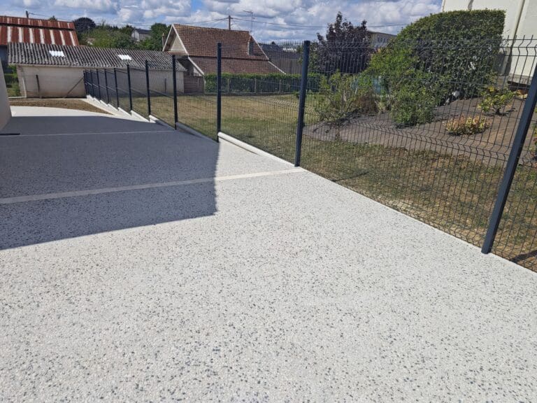 Terrasse en béton désactivé avec clôture en grillage sur pelouse et plantations