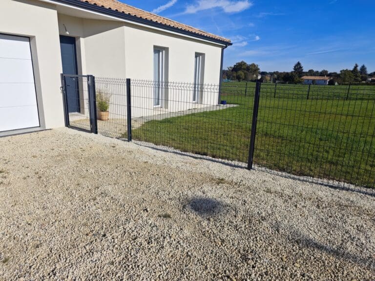 Clôture grillagée noire devant une maison avec jardin et gravier