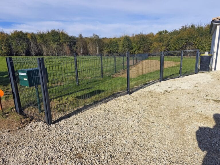 Clôture métallique noire avec portail sur terrain herbeux et allée de gravier