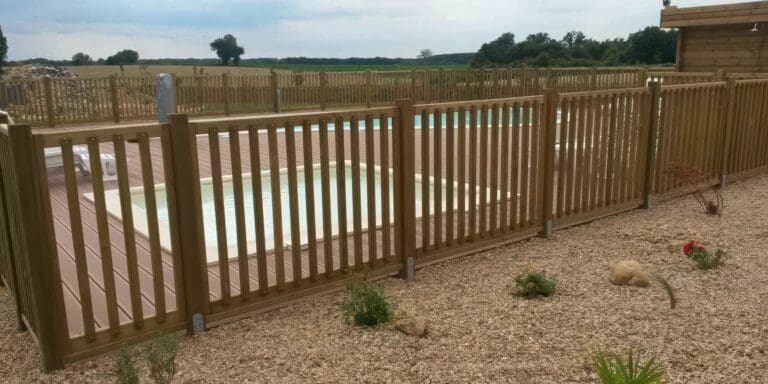 Piscine clôturée en bois avec margelles en bois et terrain gravillonné à côté
