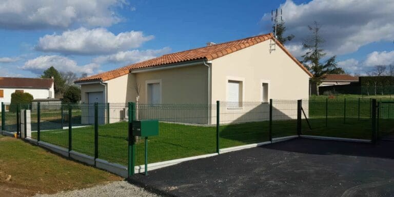 Maison avec toiture tuile et jardin clôturé par une haie verte et un portail