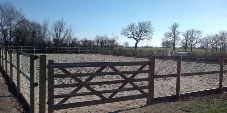 Enclos avec sol sablé entouré d'une clôture en bois et panneaux vitrés