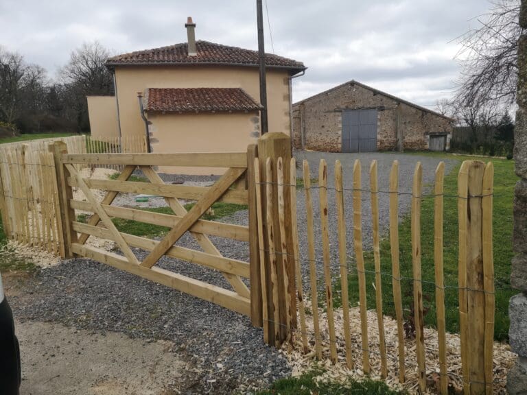 Portail et clôture en bois clair devant une maison beige avec toiture en tuiles rouges